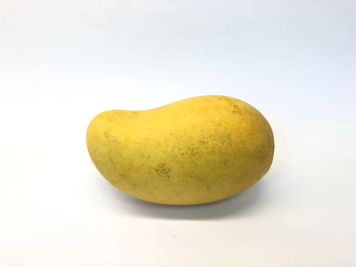 A single yellow mango on a soft blush backdrop.