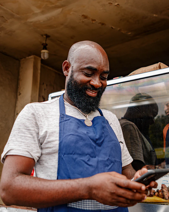 A cook in a blue apron checks his phone at a grill counter.